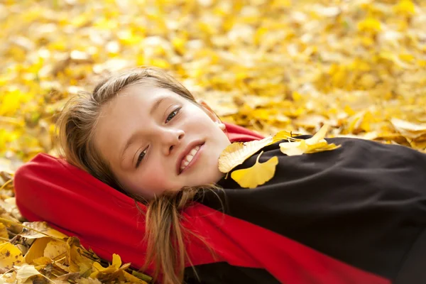 Menino sorridente em folhas de outono — Fotografia de Stock