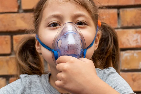 Little girl doing inhalation procedure at home using a mask