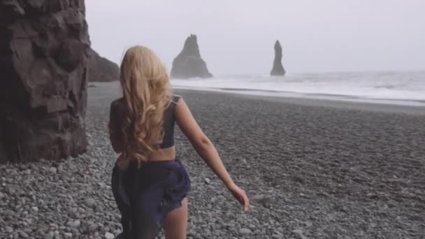 Woman with Wavy Blonde Hair Running Towards the Black Beach Shore — Stock Video