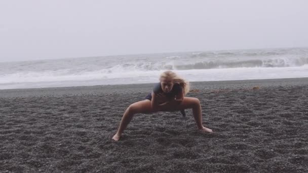 Woman with Arms Wrapped Around Her Chest and Legs in a Squat Position Dancing by the Beach — Stock Video