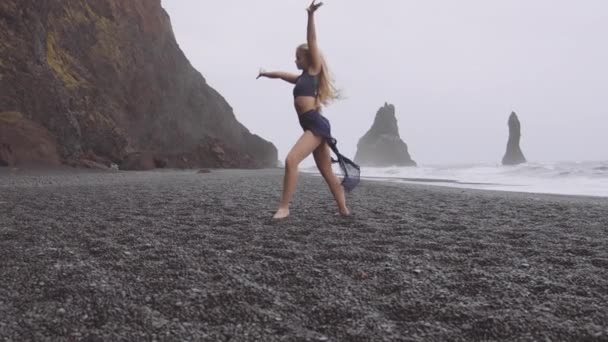 Lady in abito blu Ballando in spiaggia di sabbia nera con vista sull'oceano in background — Video Stock