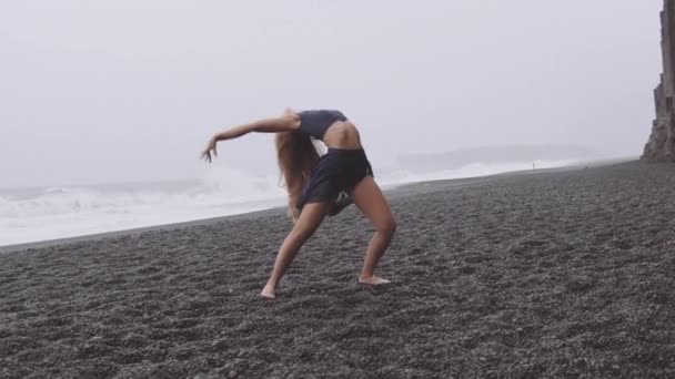 Mujer flexible y hermosa bailando junto a la playa negra en un día ventoso — Vídeos de Stock