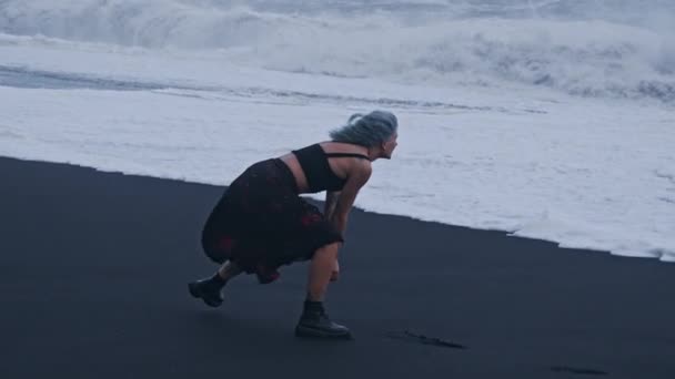 Cooles Mädchen weicht Brandung am schwarzen Sandstrand aus — Stockvideo