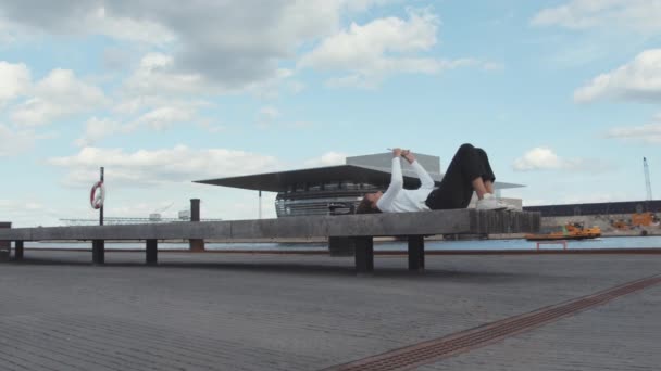 Femme allongée sur un banc prenant un selfie avec un petit bateau passant par — Video