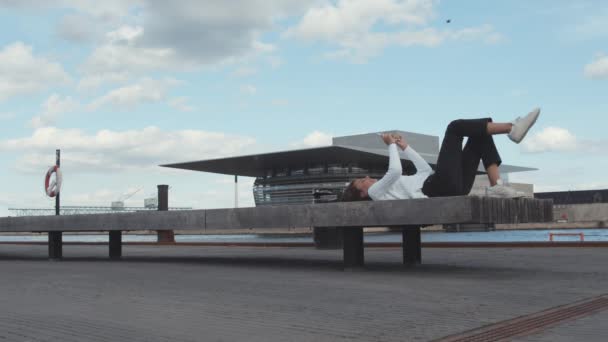 Jasná obloha, levobok a dospívající dívka ležící na lavičce s telefonem na ruce — Stock video