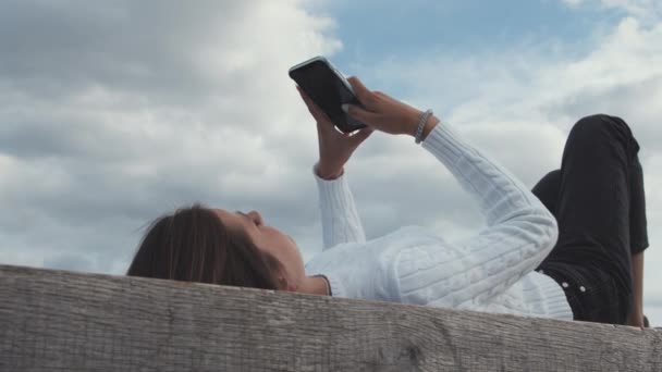 Fiatal nő a koppenhágai Portside használja a telefont, miközben feküdt a padon — Stock videók