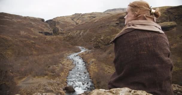 Жінка в шевелі дивиться на річку з каменів — стокове відео