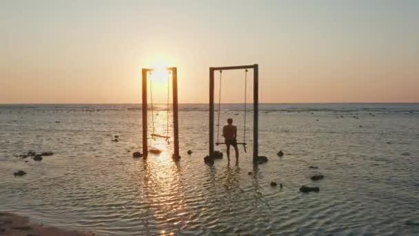 Man zit op schommel in zee bij zonsondergang — Stockvideo