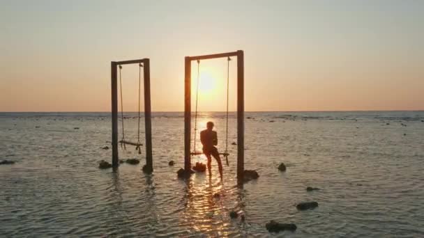 Homem no balanço ao pôr-do-sol no mar — Vídeo de Stock