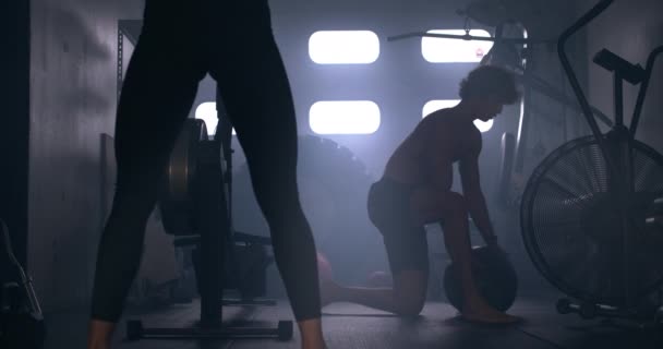 Женщина поднимает гантель, как мужчина использует медицинский мяч в спортзале — стоковое видео