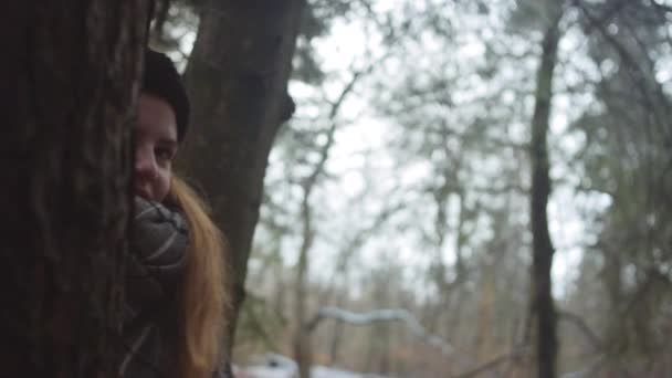 Adolescente chica en bufanda mirando desde detrás del árbol — Vídeos de Stock
