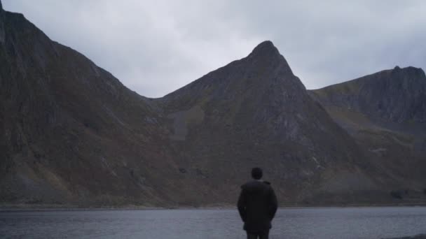 Человек, стоящий на скалах и смотрящий через фьорд — стоковое видео