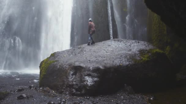 Donna accovacciata sulla roccia per vedere la cascata — Video Stock