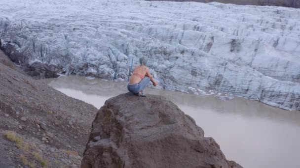 Drone sopra donna su roccia guardando ghiacciaio — Video Stock