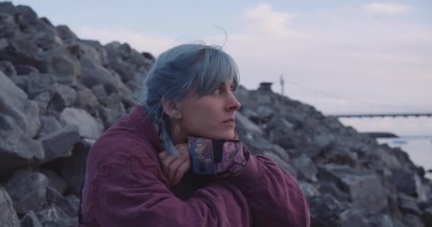 Przemyślana dziewczyna z niebieskimi włosami siedzi na lodowcu — Wideo stockowe