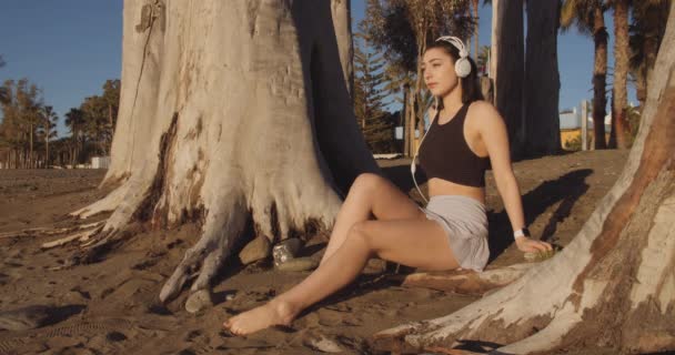 Жінка в навушниках відпочиває на пляжі — стокове відео