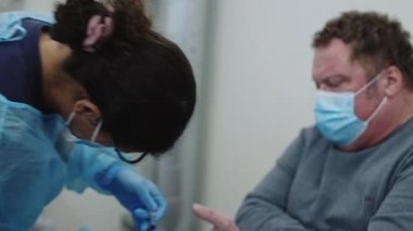 Doktor önlüklü ve maskeli, kan örneği alıyor.