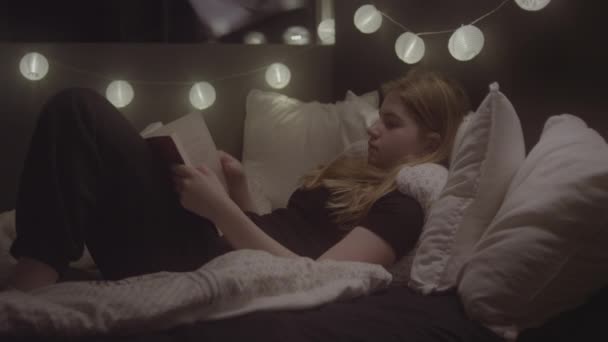 Teenage Girl Relaxing On Bed And Reading Book — Stockvideo