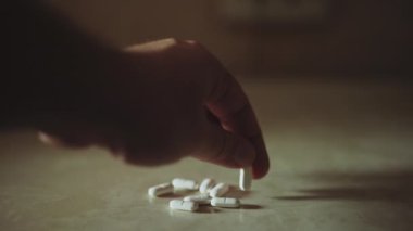 Masanın üstüne haplar ve bir adam başka bir tablet yerleştiriyor.