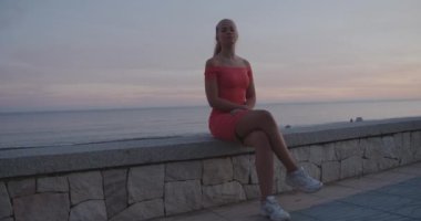 Şeftali Elbiseli Kadın Sahilde Bacak bacak üstüne atmış bir şekilde oturuyor