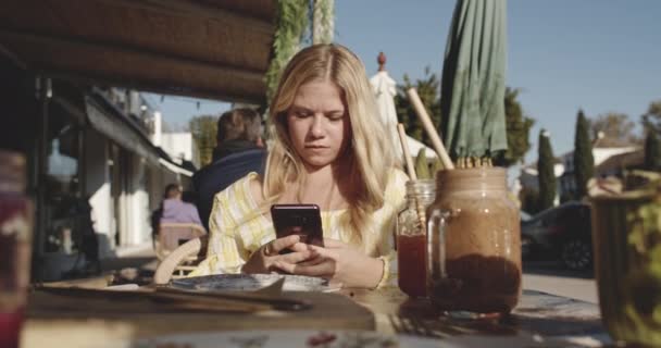 Kvinna Använda Smartphone som hon väntar på restaurang bord utanför på en solig dag — Stockvideo