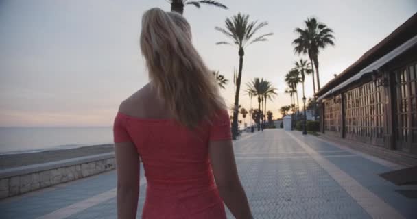 Junge Frau spaziert bei Sonnenuntergang an der Strandpromenade — Stockvideo