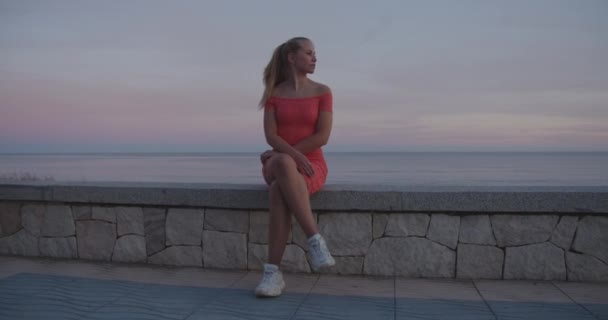 Vrouw zittend met benen gekruist door de betonnen bank en panoramisch uitzicht op de oceaan — Stockvideo