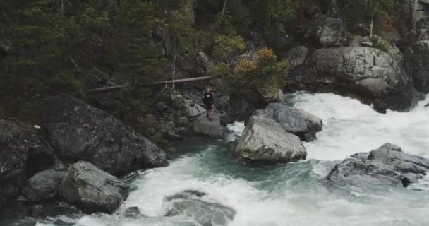 Підліток, що стоїть по скелях по сусідству з річкою — стокове відео