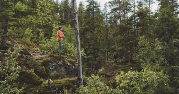 Niño con capucha naranja de pie sobre rocas en el bosque verde — Vídeo de stock