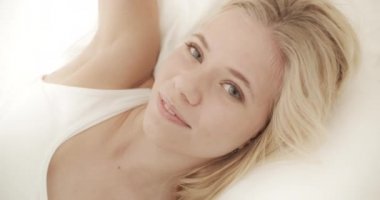 Beyaz çarşaflarla yatağında yatarken Alaycı Gülümseyen Kadın