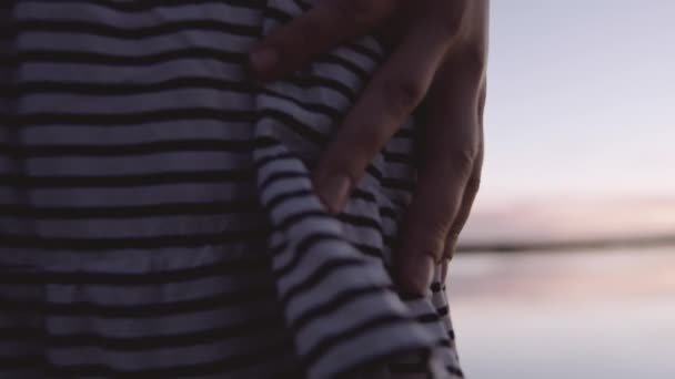 Vrouw grijpen gestreepte jurk door het water bij zonsondergang — Stockvideo