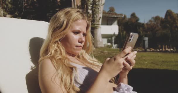 Блондинка смс на смартфоне в солнечном саду — стоковое видео