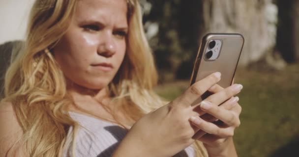 Mensajes de texto de la mujer en el teléfono inteligente en Sunny Garden — Vídeo de stock