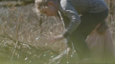 Kız kabarcıklar üflerken, erkek kardeş onları patlatıyor.