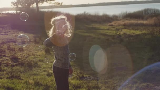 Chłopiec stojący na słonecznym polu i dmuchający w bąbelki różdżką — Wideo stockowe