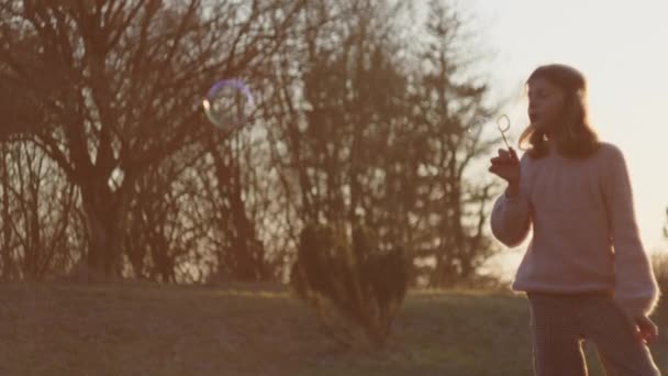 Jong meisje blazen bubbels in zonsondergang veld — Stockvideo