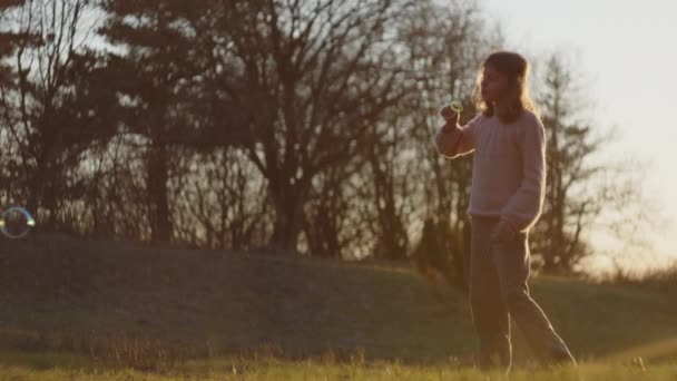 Κορίτσι φυσάει φυσαλίδες και κυνηγώντας τους στο ηλιοβασίλεμα — Αρχείο Βίντεο