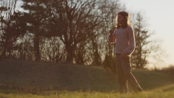 Νεαρό κορίτσι φυσάει φυσαλίδες στο πεδίο ηλιοβασιλέματος — Αρχείο Βίντεο