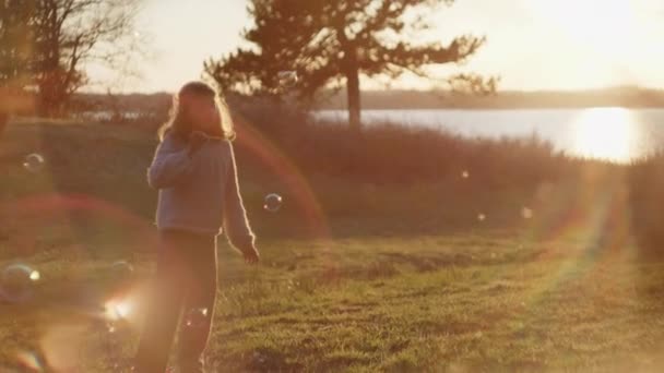 Κορίτσι φυσάει φυσαλίδες στο πεδίο στο ηλιοβασίλεμα — Αρχείο Βίντεο