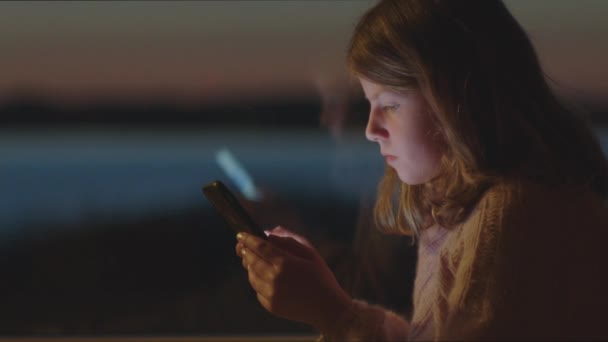 Ung flicka spelar på smartphone i skymningen — Stockvideo