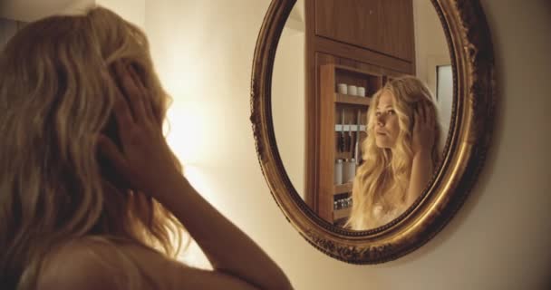 Молодая женщина смотрит на свое отражение в зеркале — стоковое видео