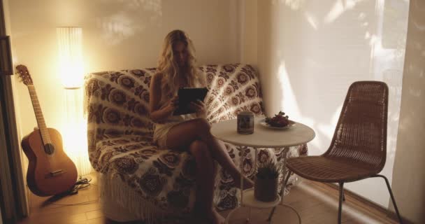 Piękna kobieta na kanapie Czytanie Tablet i picie kawy — Wideo stockowe