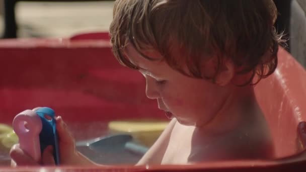 Menino brincando com brinquedos no banho ao ar livre — Vídeo de Stock