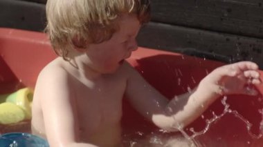 Çocuk su içinde oyuncak tırmıkla oynuyor ve su sıçratıyordu.