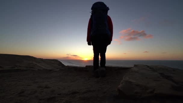 Турист с рюкзаком наблюдая закат с пляжа — стоковое видео