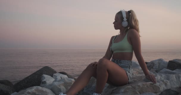 Relaxing Woman Sitting By Sea Wearing Headphones — Video Stock