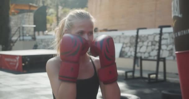 Kvinde boksesæk i boksehandsker på udendørs gym – Stock-video
