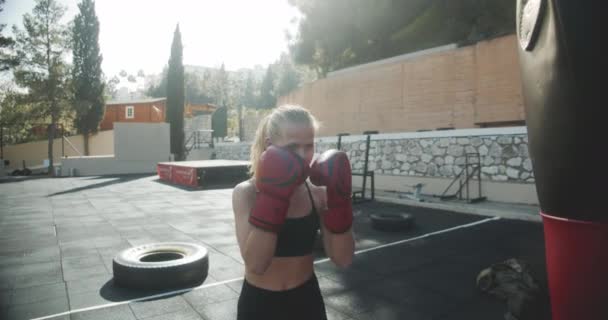 Жінка пробиває сумку в бокс рукавички на відкритому повітрі тренажерний зал — стокове відео
