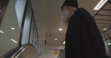 Sakallı Erkek Gezgin yürüyen merdivenden inerken kendi kendine konuşuyor.