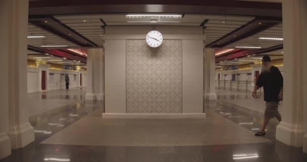 Hombre caminando en el marco en una estación de tren bien iluminada con reloj en el centro — Vídeo de stock
